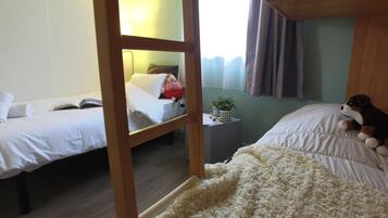 Una habitación con dos camas, una mesita con una planta y un peluche sobre una de ellas.