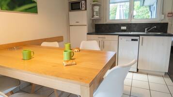 A compact kitchen with a wooden table, white chairs, a microwave, a coffee maker, and a dishwasher.