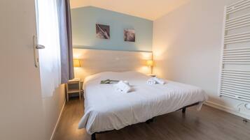 Un lit bien fait, avec du linge de lit blanc, une table de chevet avec une lampe et deux tableaux accrochés au mur.