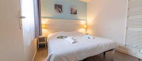 A neatly made bed with white linens, a bedside table with a lamp, and two wall-mounted pictures.