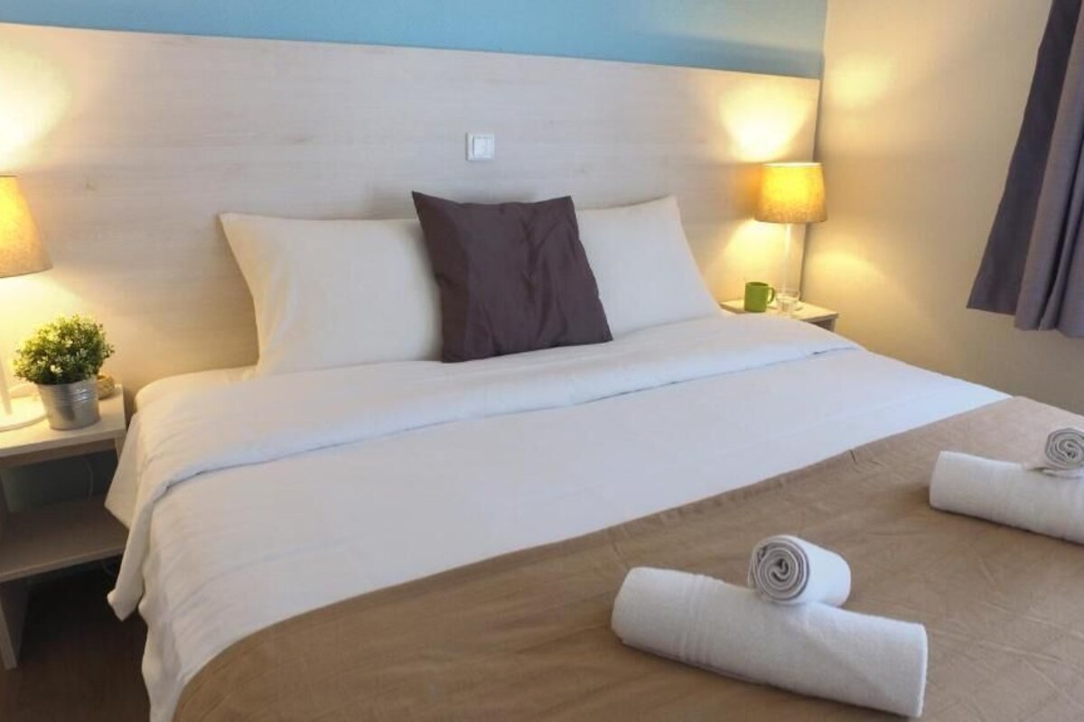 Ein Hotelzimmer mit Bett, zwei Nachttischlampen, einem Nachttisch mit Pflanze und einem Fenster mit Vorhängen.