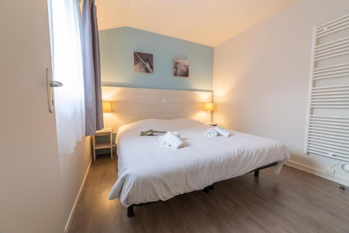 Ein Hotelzimmer mit Bett, zwei Nachttischlampen, einem Kopfteil und einem Fenster mit Jalousien.