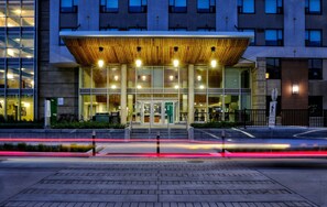 A modern building with a wooden canopy entrance, large glass windows, and a visible sign indicating a parking area. - Residence & Conference Centre - Ottawa West (Ottawa)