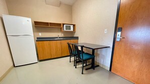 A compact kitchen with a refrigerator, microwave, wooden cabinets, a sink, and a dining table with chairs. - Residence & Conference Centre - Ottawa West (Ottawa)