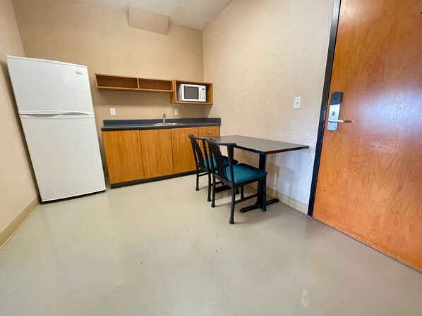 A compact kitchen with a refrigerator, microwave, wooden cabinets, a sink, and a dining table with chairs. - Residence & Conference Centre - Ottawa West (Ottawa)