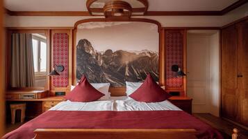 Une chambre d’hôtel avec un grand lit, deux lampes de chevet, une tête de lit en bois, une grande fenêtre avec des rideaux et une fresque murale représentant un paysage de montagne.