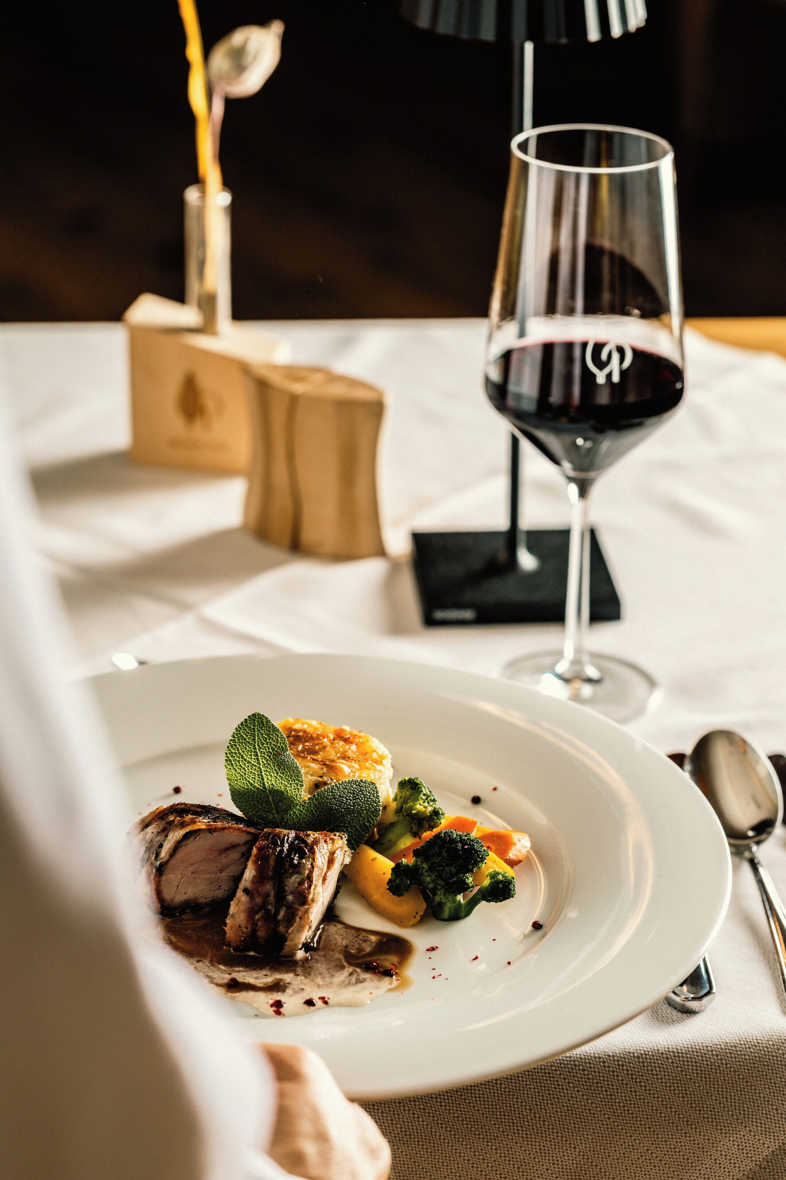 A dining table with a plate of food, a glass of red wine, and a candle.