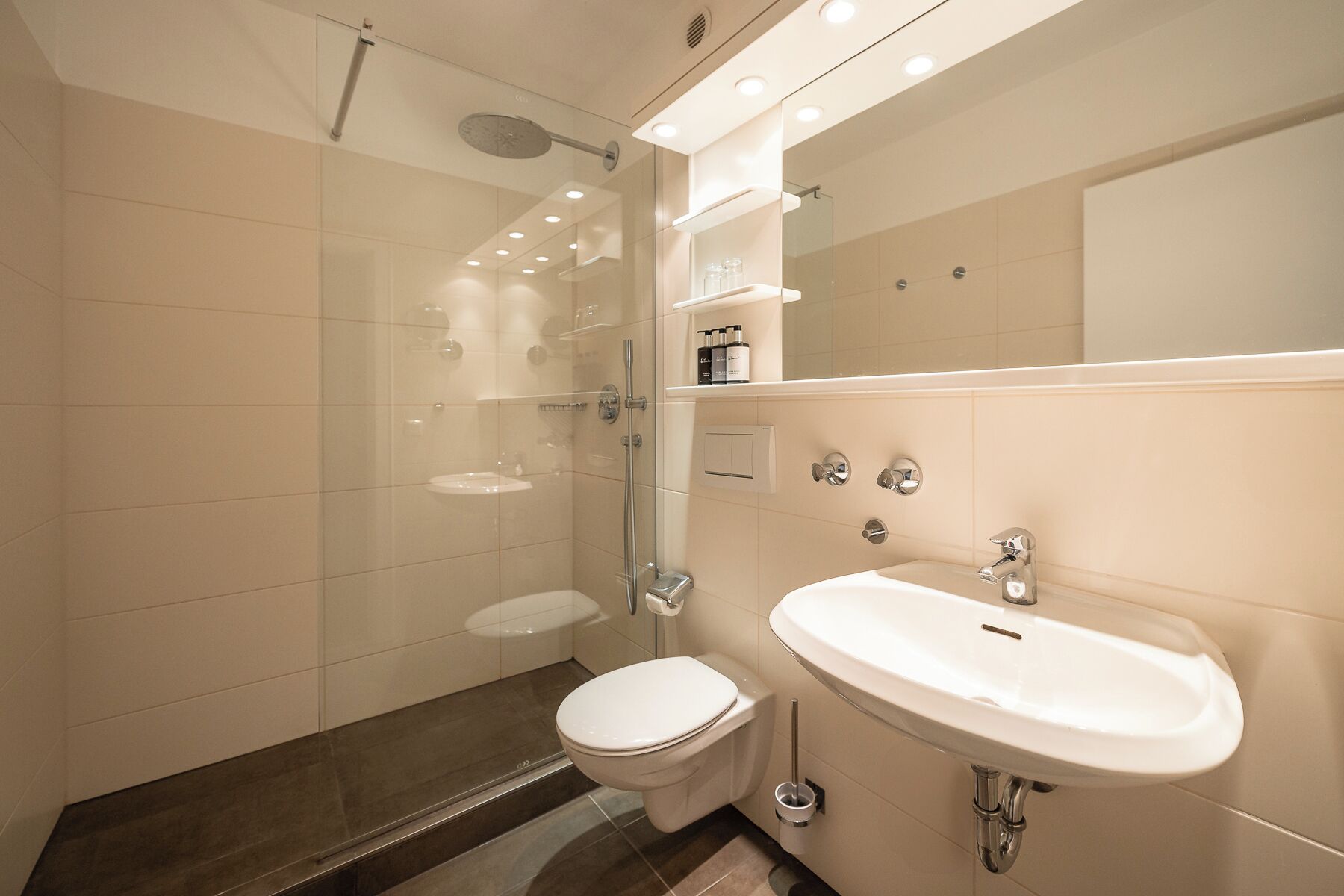 Un baño moderno con cabina de ducha de vidrio, inodoro blanco y lavamanos con espejo.