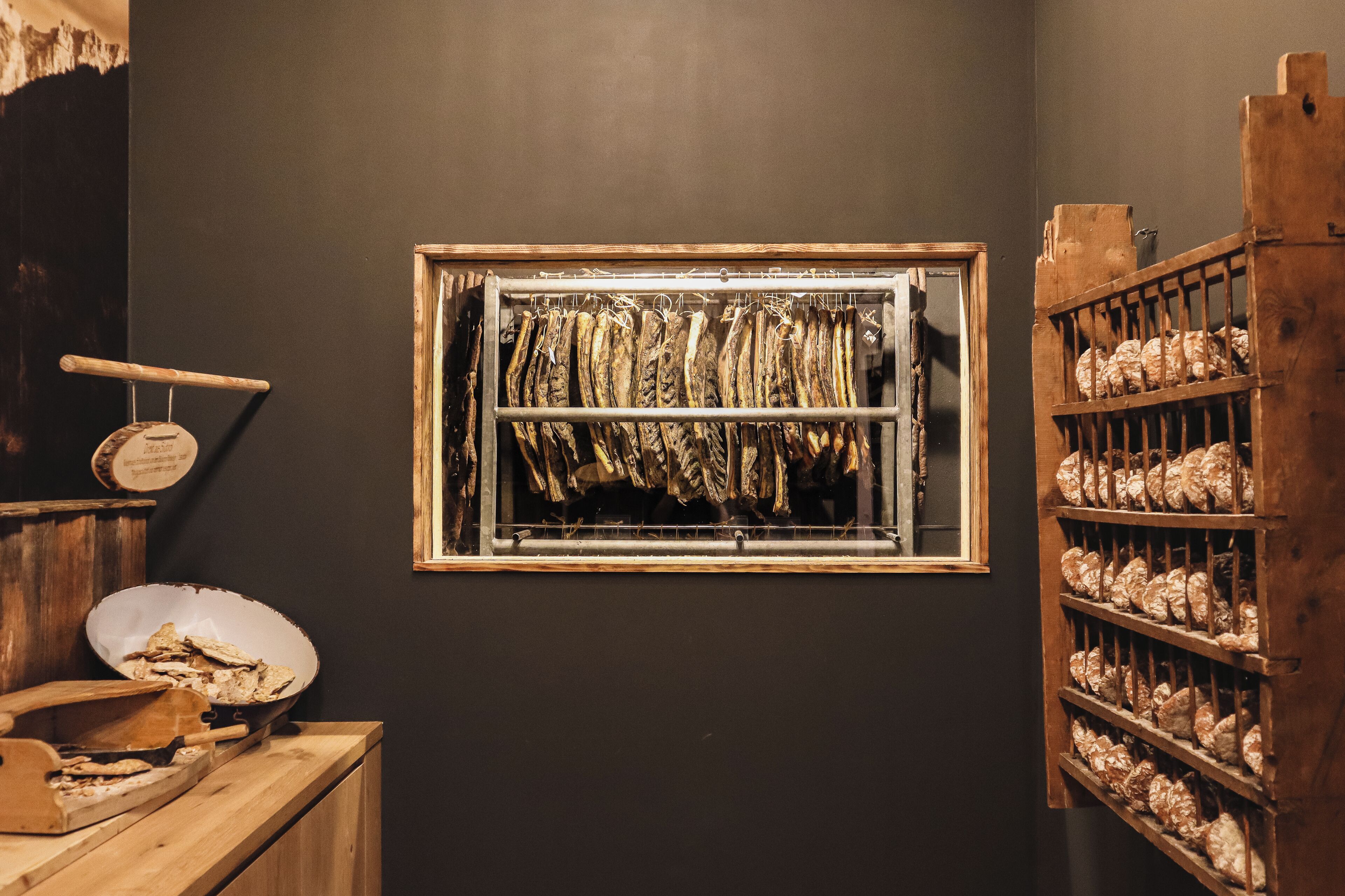 Ein Zimmer mit einem Holzboden, auf dem getrockneter Fisch liegt, einem Holzgestell mit mehr getrocknetem Fisch und einem Fenster, vor dessen Scheibe getrockneter Fisch hängt.