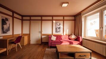 A room with a wooden floor, a red sofa, a wooden coffee table, a desk, and framed pictures on the wall.