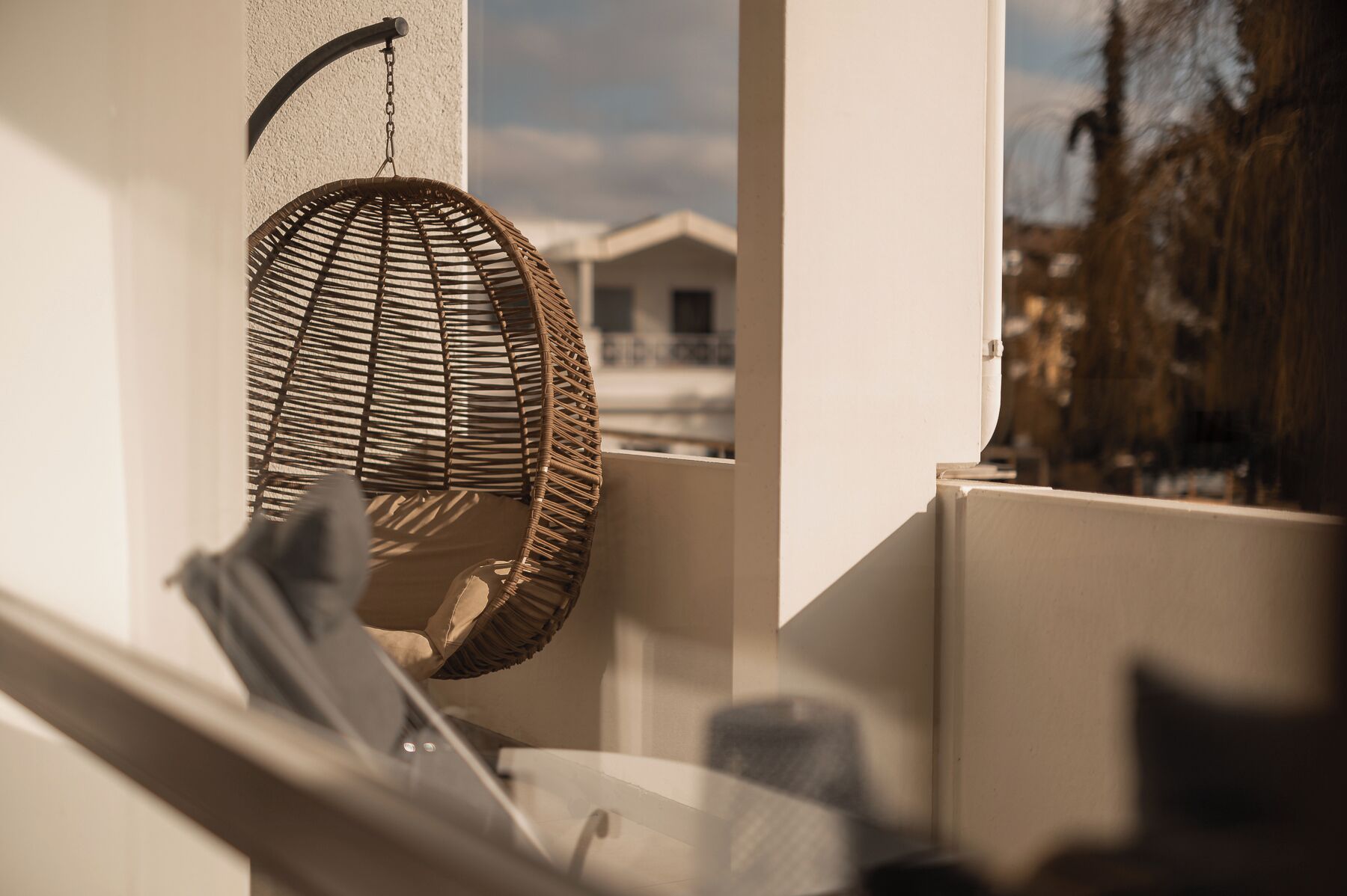 A wicker chair hanging by a wall, a window with a view of buildings, and a partial view of a room's interior.