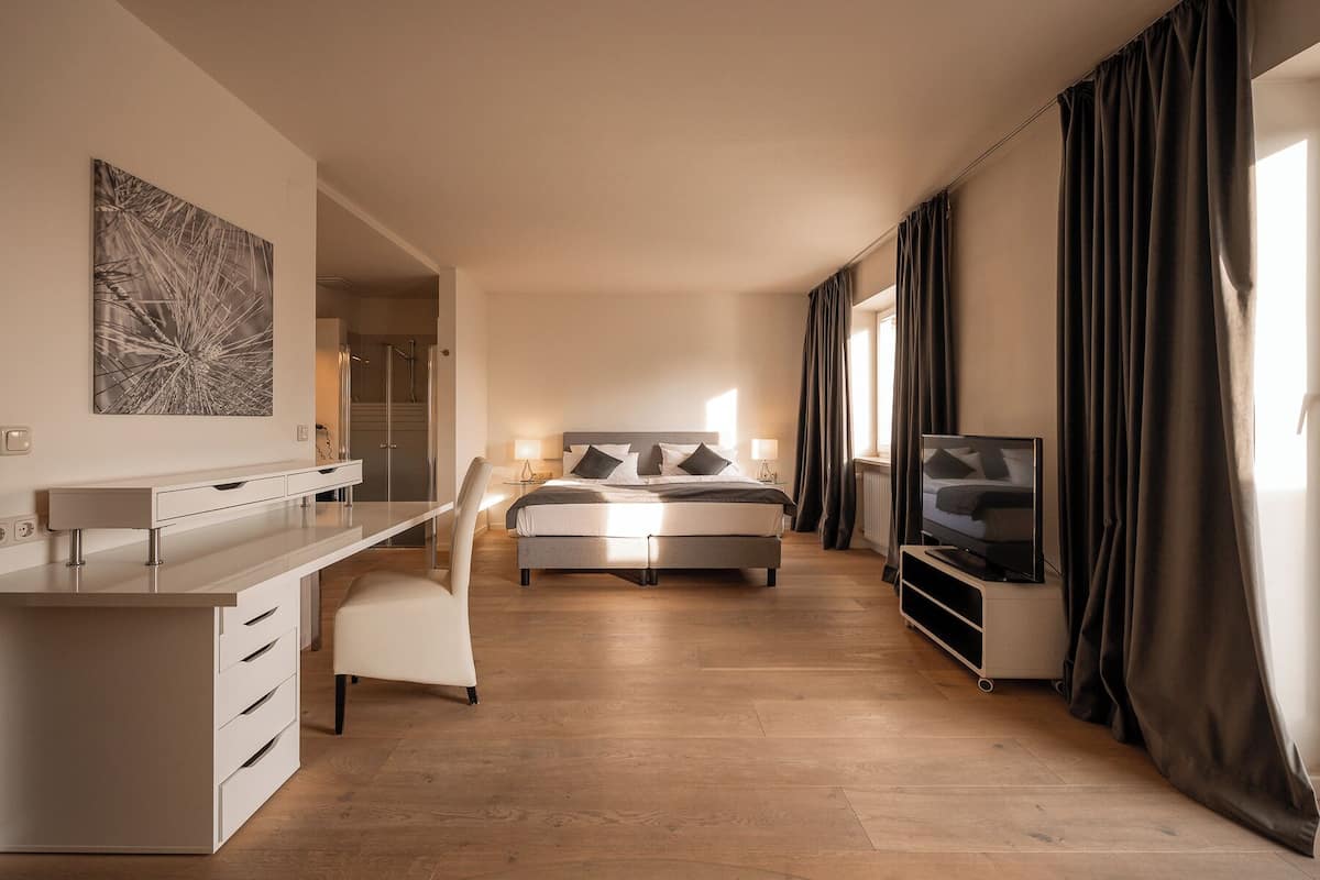 Una habitación de hotel moderna con cama, escritorio, televisor y zona de ducha.