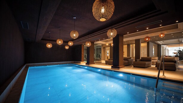 En swimmingpool med flere hængende, runde lysarmaturer, et opholdsområde med sofaer, og en åben dør til et andet rum.