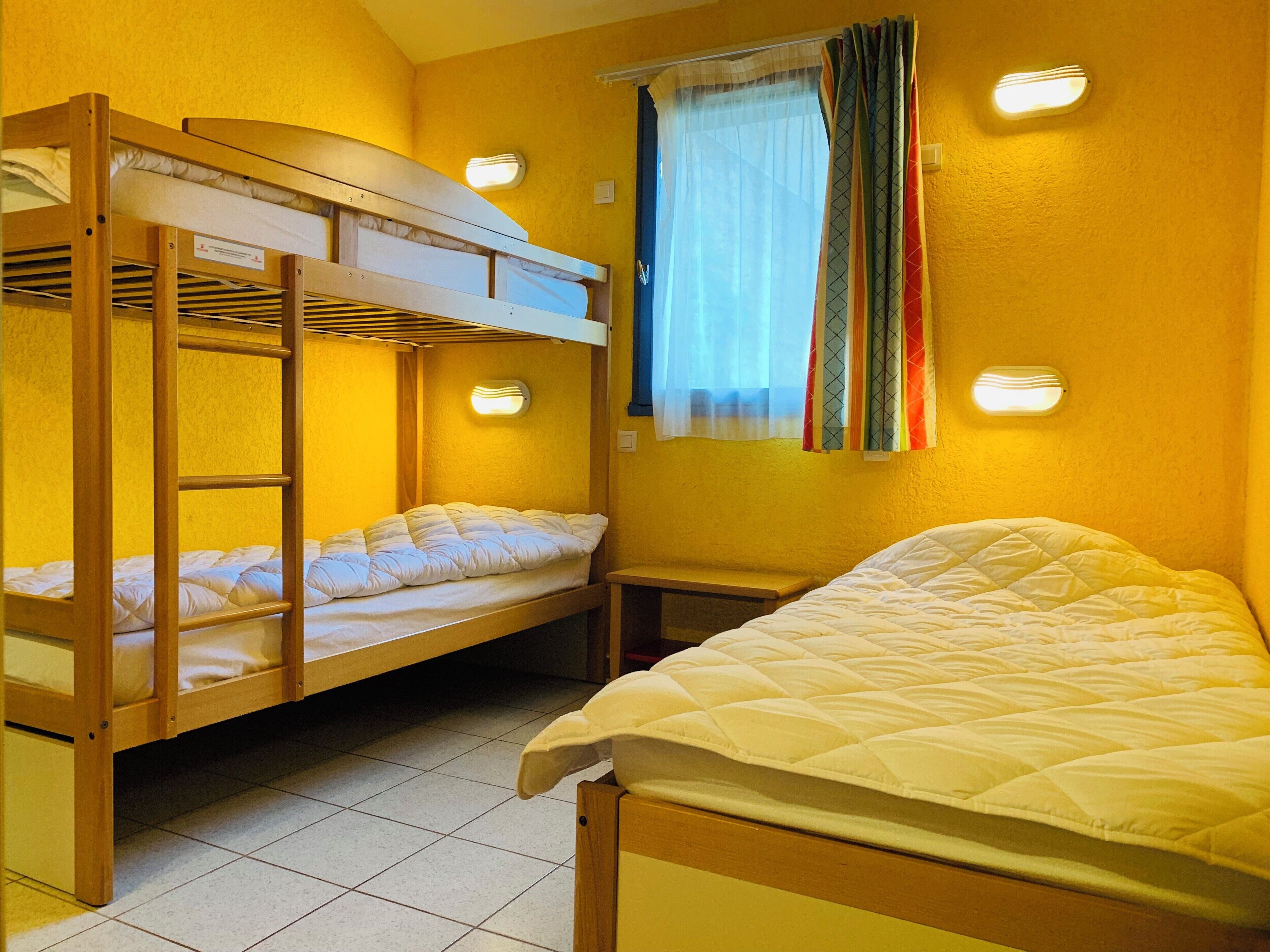 Una camera del dormitorio con letti a castello, un letto singolo e una finestra con tende.