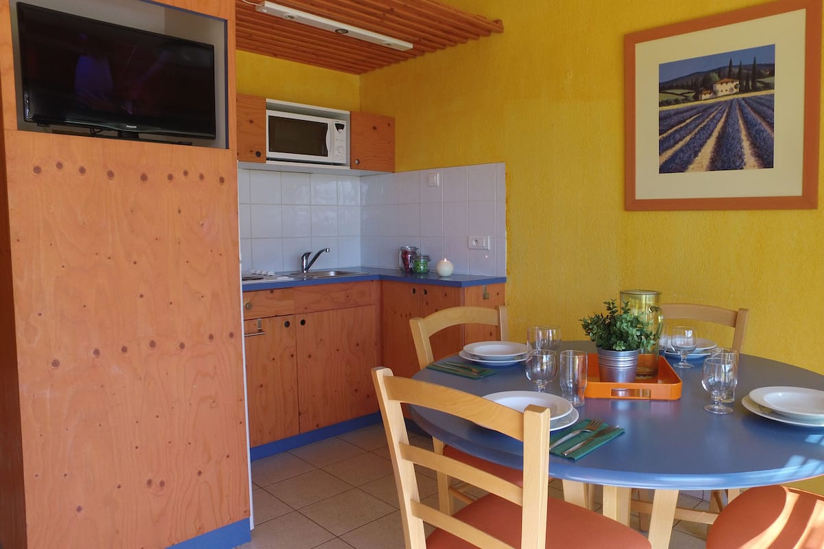 A dining area with a blue table, wooden chairs, and a yellow wall.