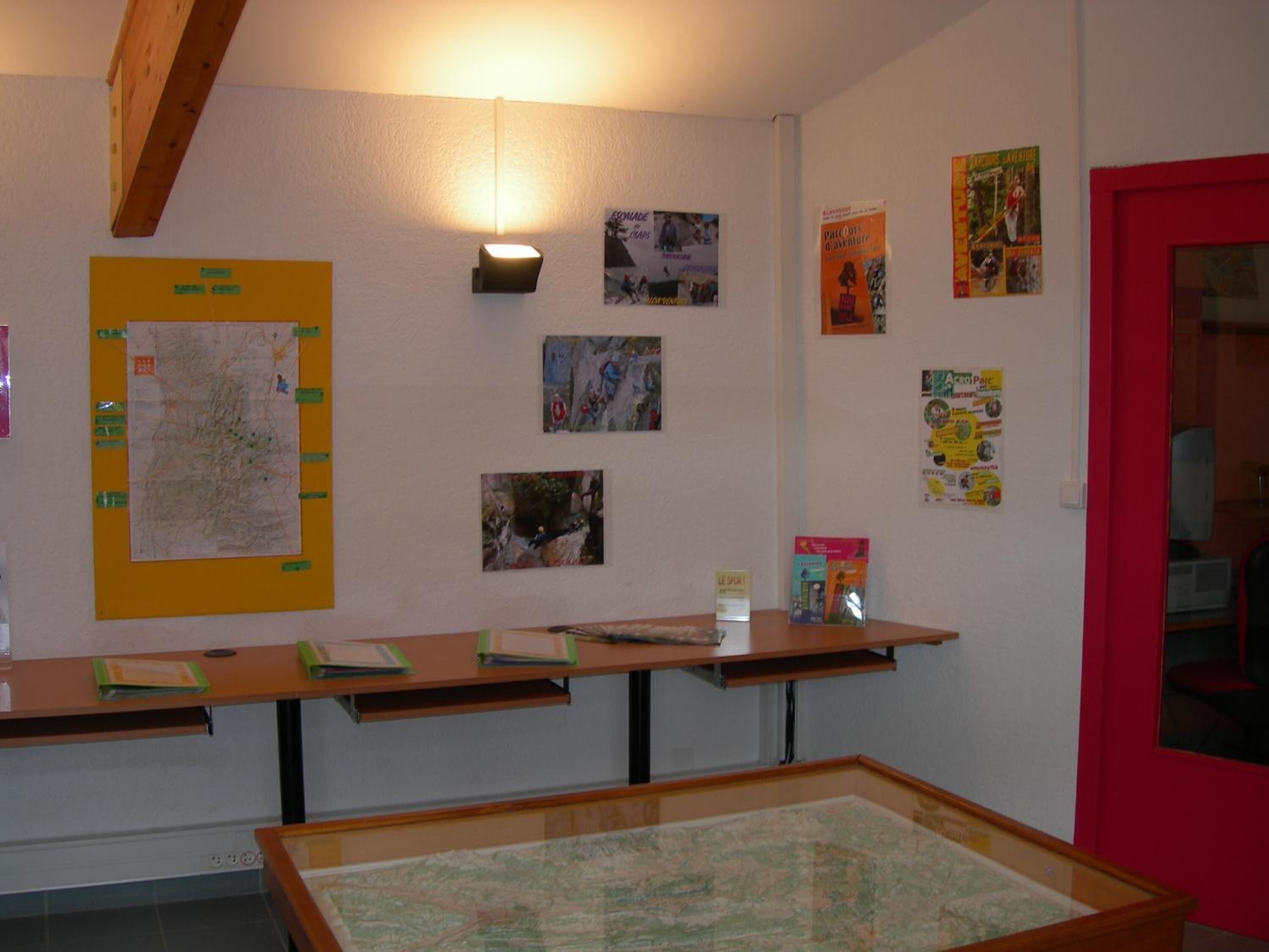 Une pièce avec un bureau en bois, une carte accrochée au mur et divers affiches.