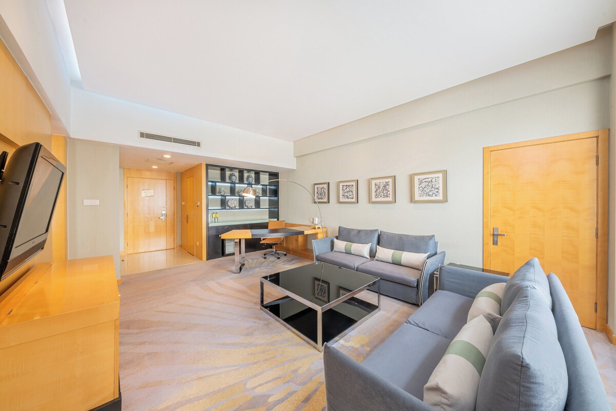 A modern living room with a sofa, a coffee table, and a TV. There is a kitchen area with a dining table and chairs.