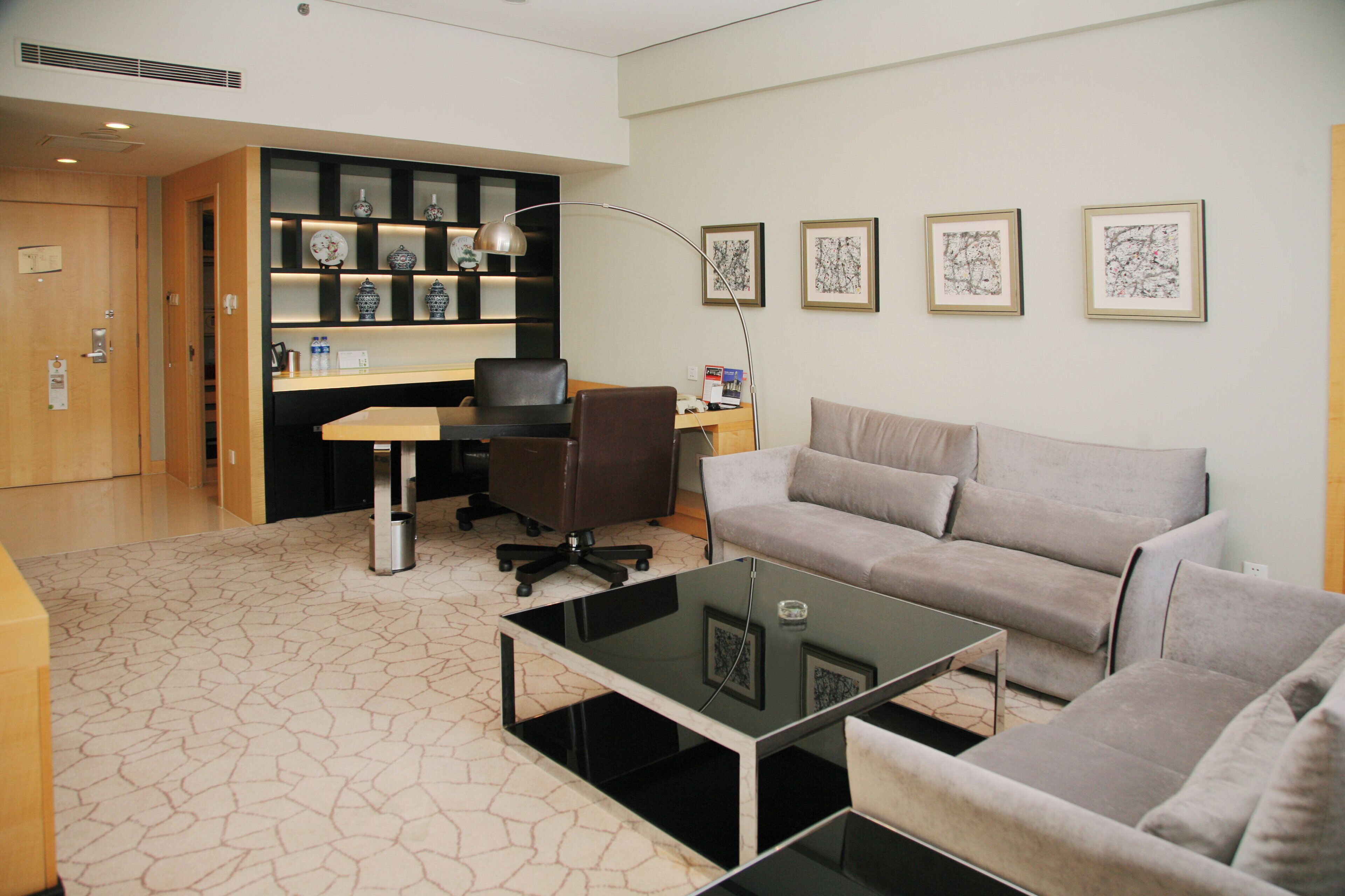 A modern living room with a glass coffee table, a sofa, a desk with a computer, and a bookshelf with decorative items.