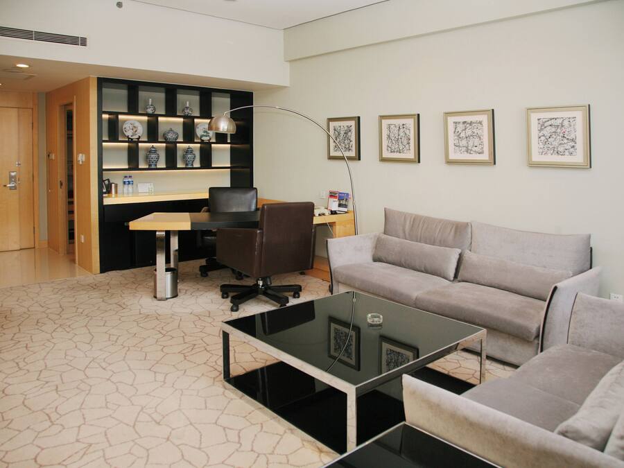 A modern living room with a glass coffee table, a sofa, a desk with a computer, and a bookshelf with decorative items.