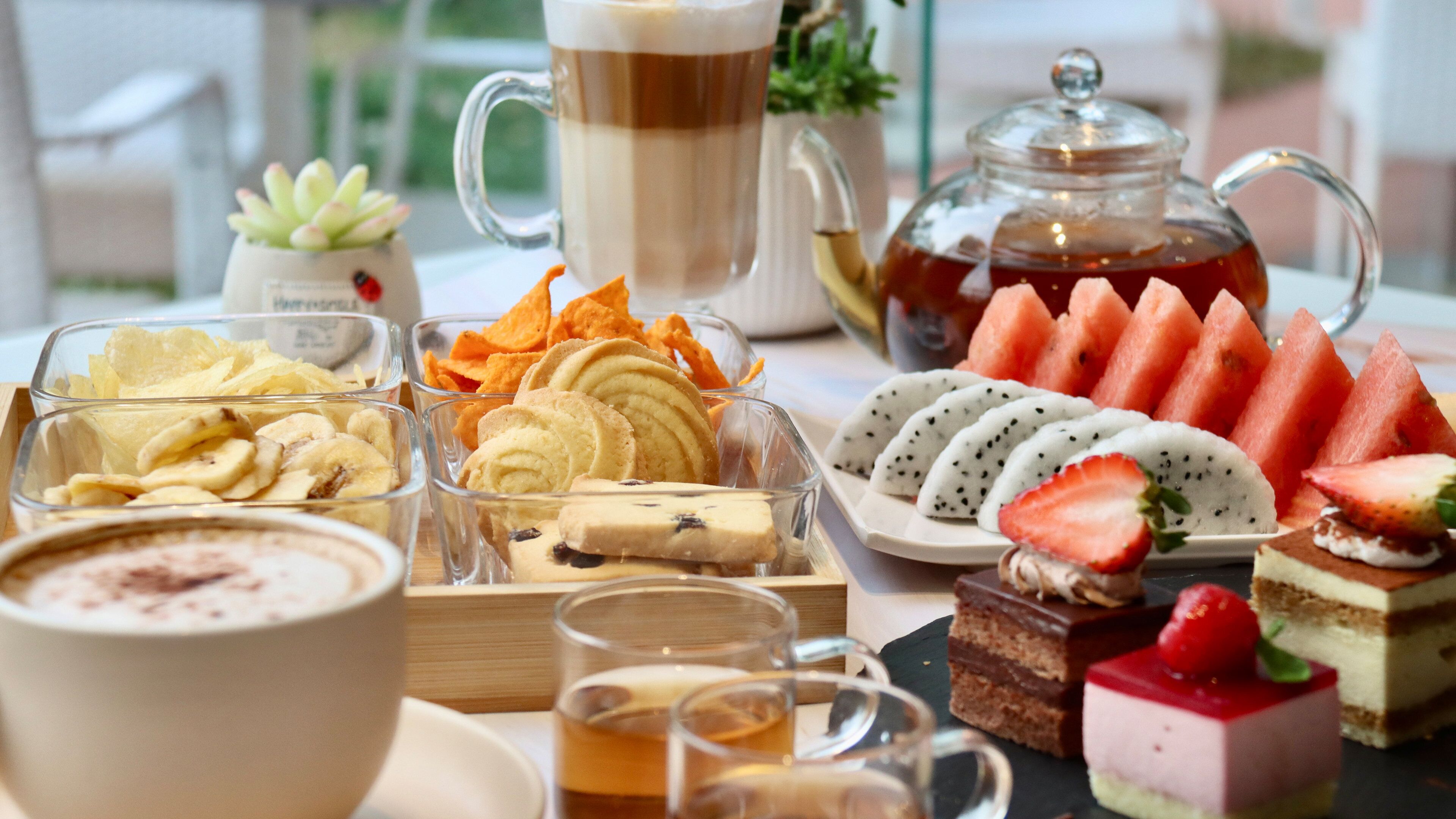 A table with various food items and beverages, including a pitcher of tea, a cup of coffee, and several desserts.