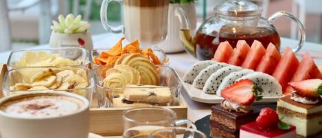A table with various food items and beverages, including a pitcher of tea, a cup of coffee, and several desserts.