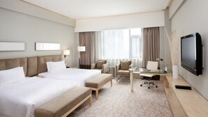 Quarto de hotel com duas camas, uma escrivaninha, uma cadeira, uma televisão e uma janela com cortinas.