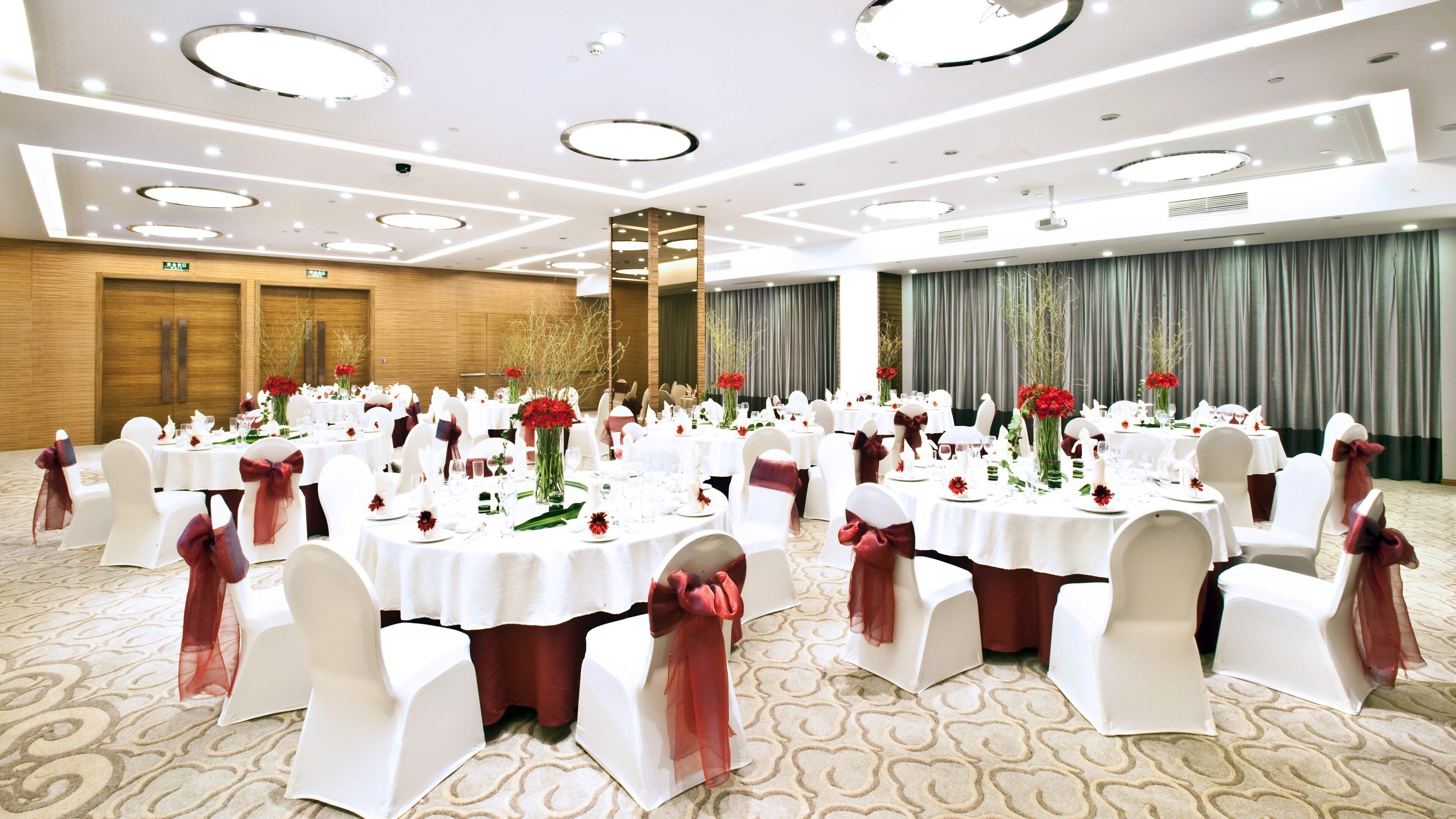 Une salle de banquet avec des tables rondes, des chaises blanches et des rubans rouges.
