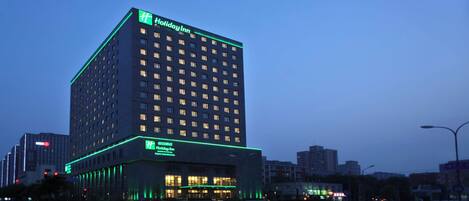 A Holiday Inn hotel with a modern design, featuring a prominent logo at the top and illuminated signage.