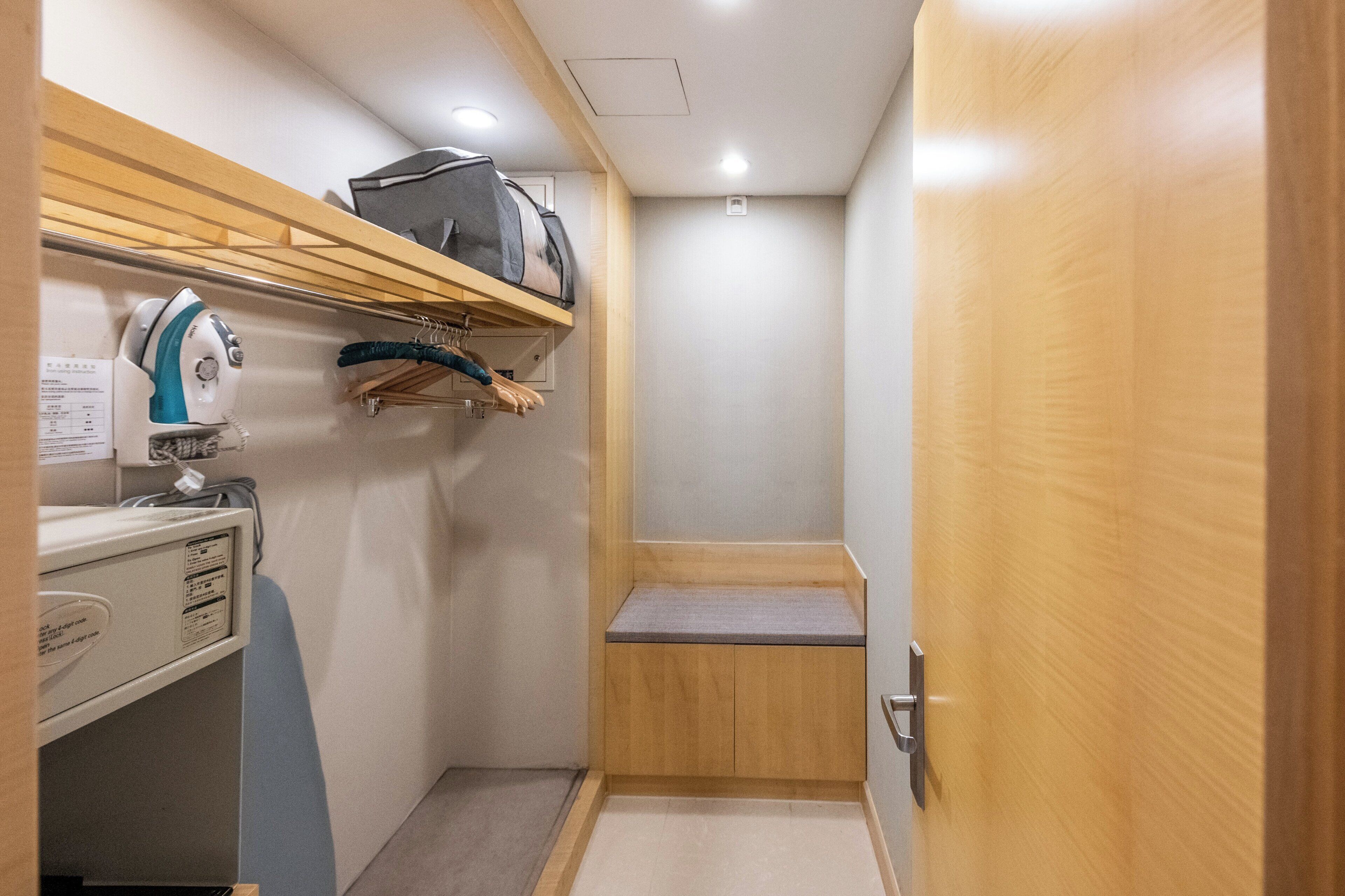 A compact bathroom with a wooden vanity, a towel rack, and a shelf with a bag.