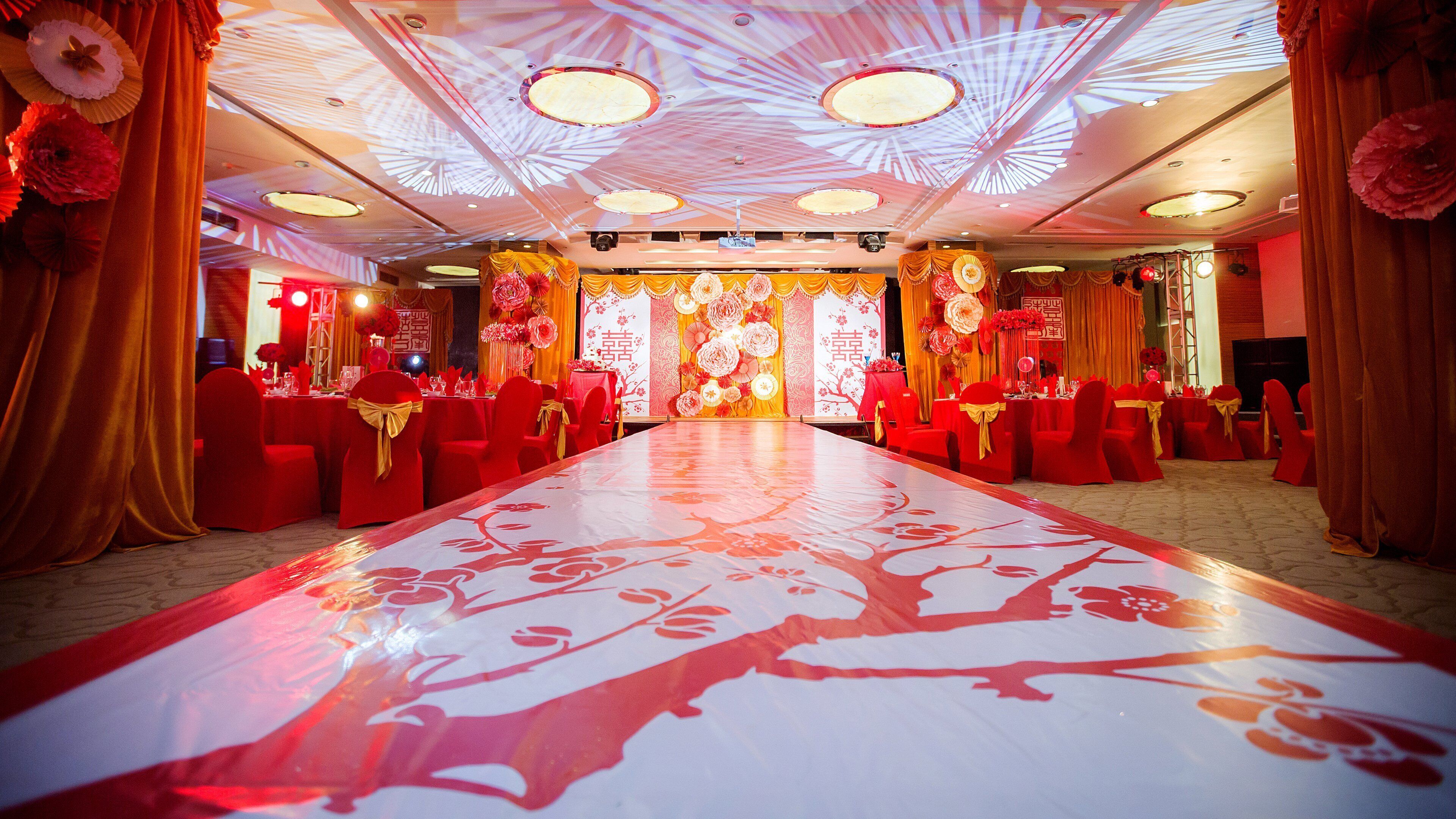 Un salón de banquetes con una larga mesa, sillas rojas y lazos dorados.