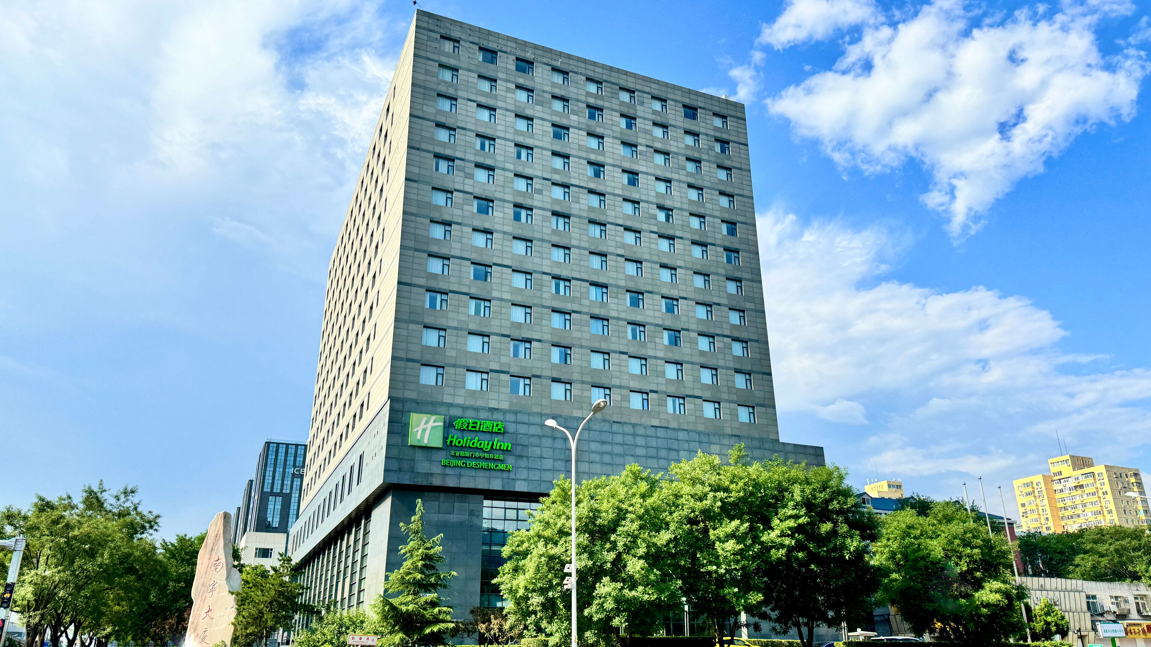A tall hotel building with a Holiday Inn sign, surrounded by trees and other buildings.