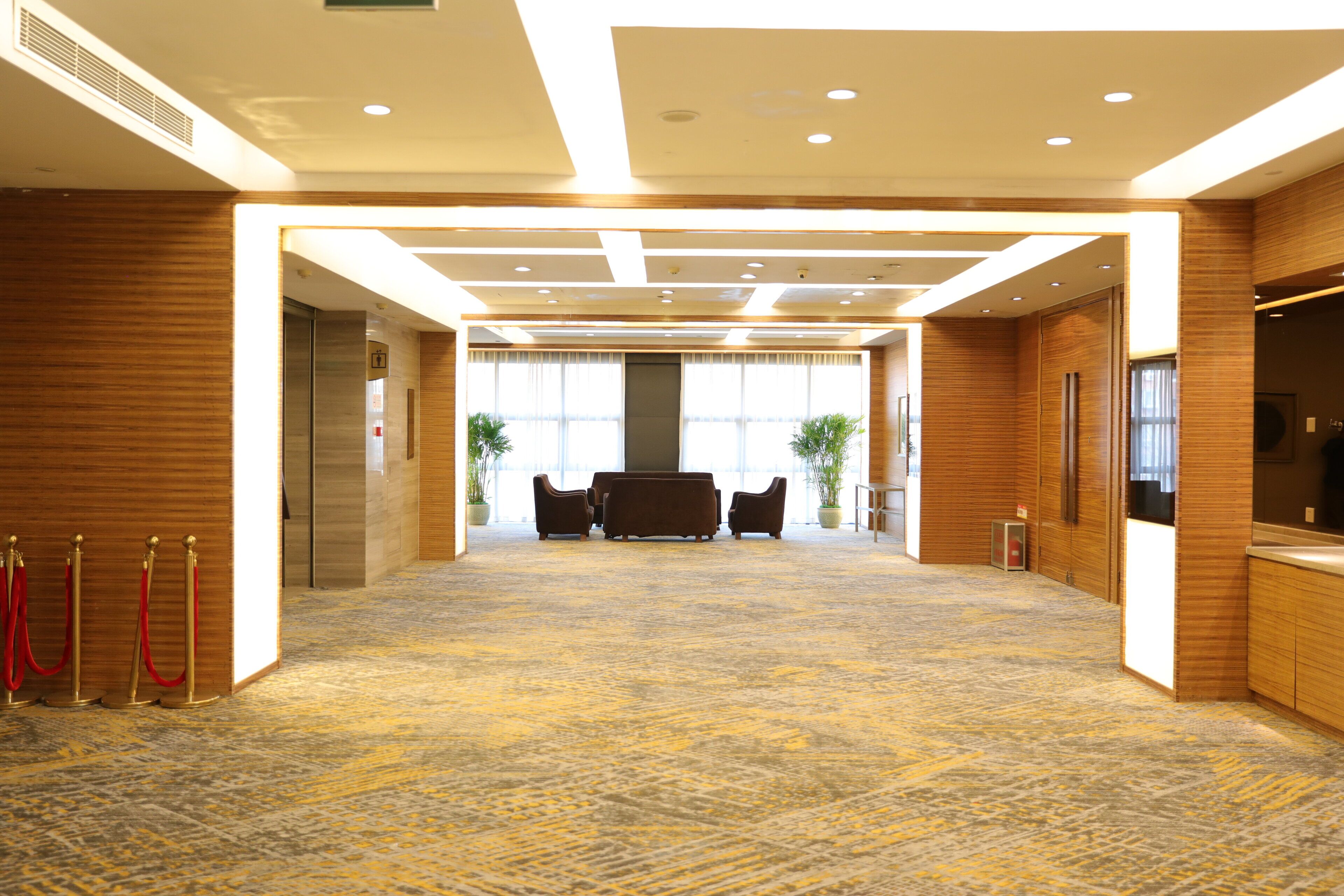 A spacious lobby with a carpeted floor, wooden paneling, a reception desk, and a seating area with two sofas.