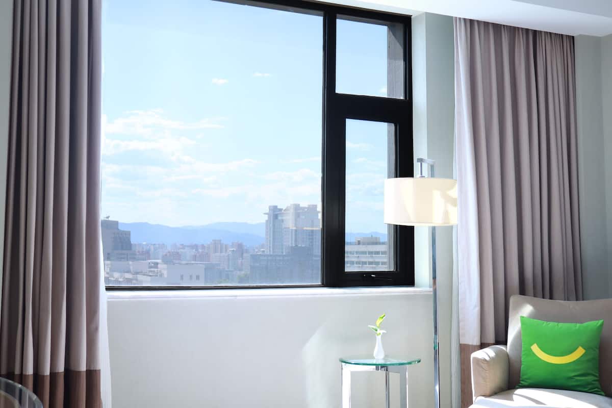 A hotel room with a large window, a lamp, a chair, and a small table.