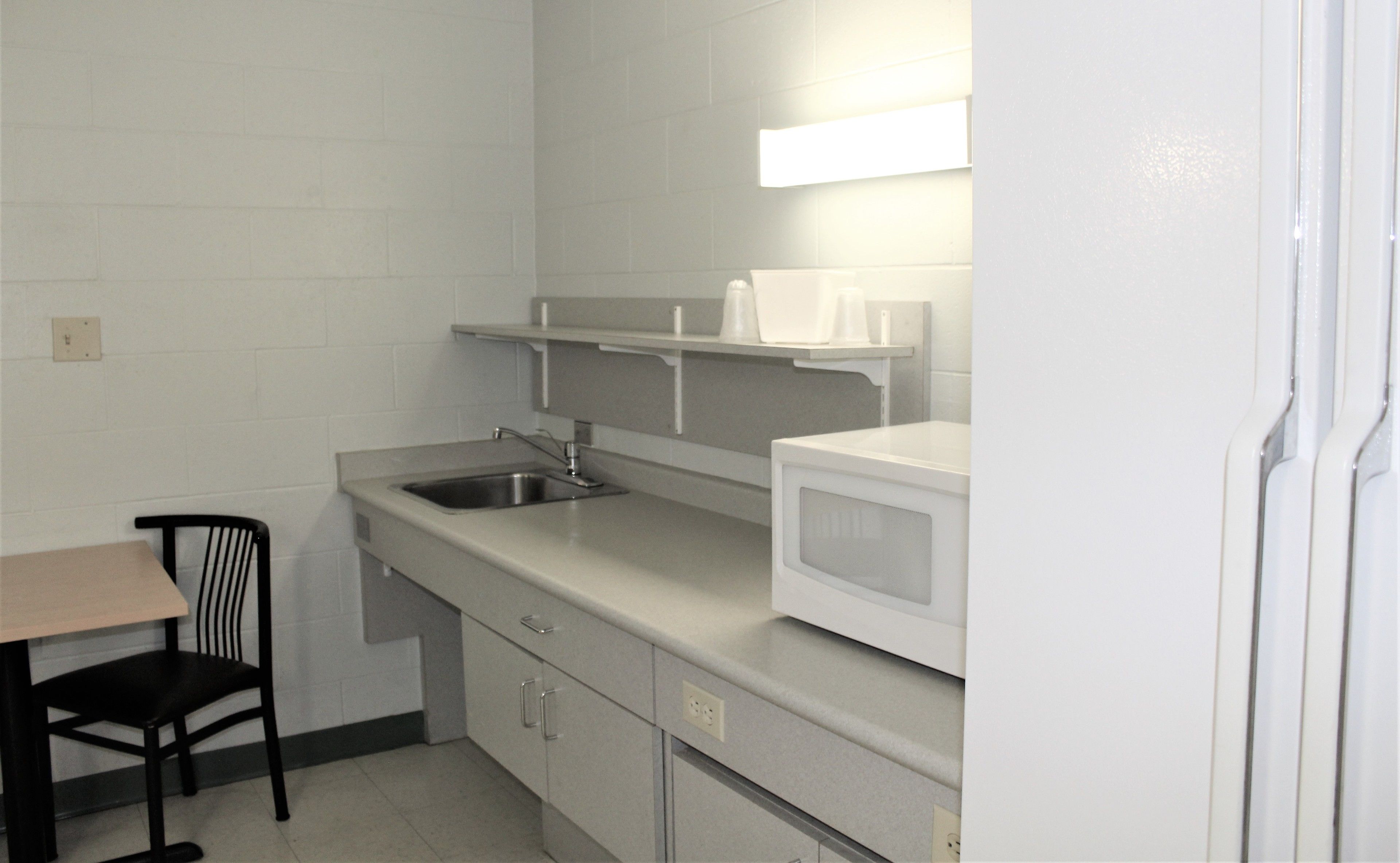 A small kitchenette with a microwave, sink, and a chair.