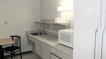 A small kitchenette with a microwave, sink, and a chair.