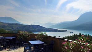 Une terrasse avec des tables et des chaises donnant sur un lac et des montagnes.