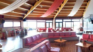 Un espace intérieur spacieux avec des bancs et des tables rembourrés de coussins rouges, de grandes fenêtres et une structure de plafond en bois.