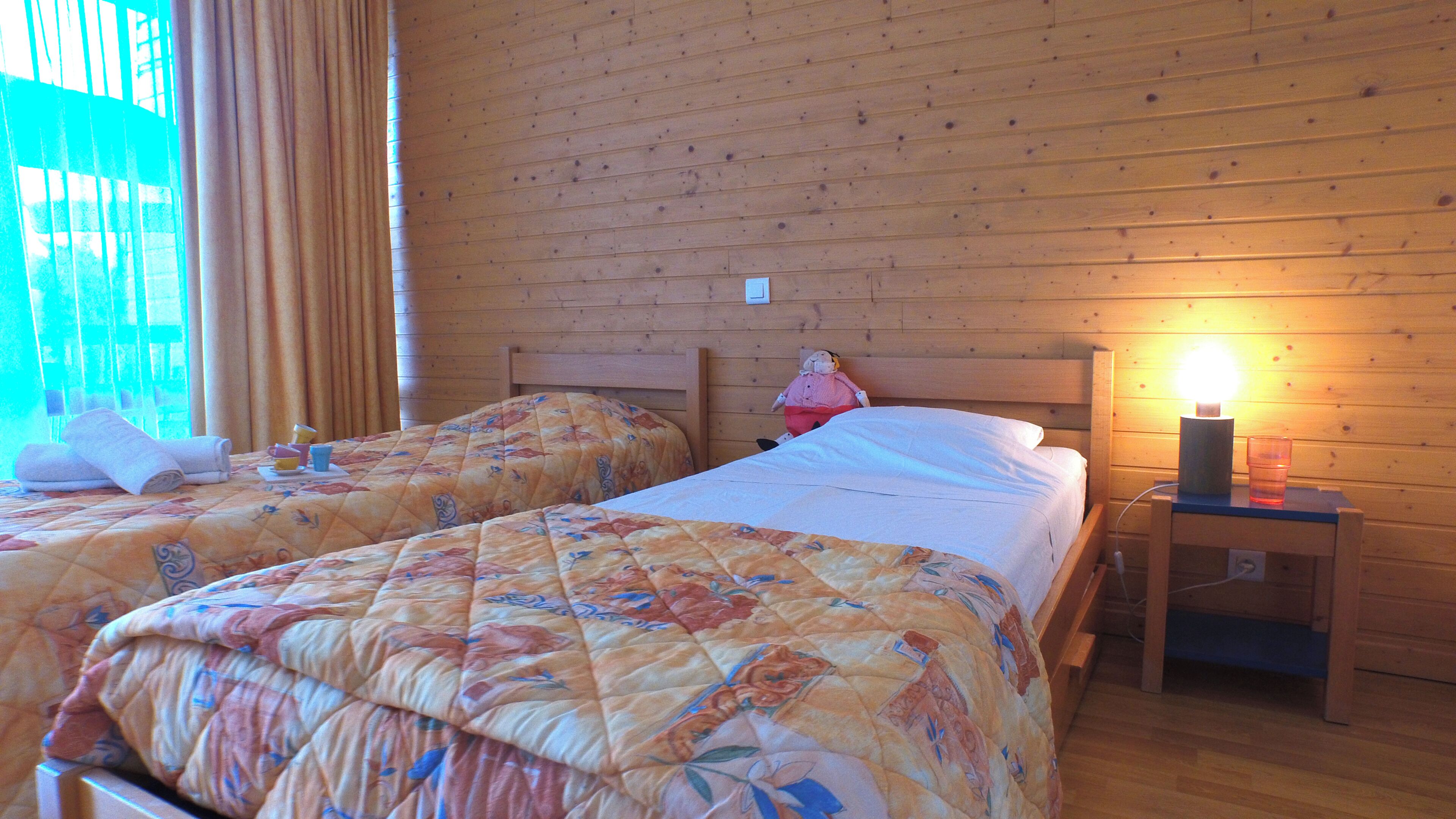 Two single beds with floral bedding, wooden headboards, a nightstand with a lamp, and a window with curtains.