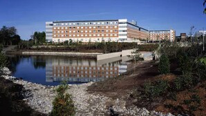 Un albergo con un grande edificio, una piscina a specchio e vegetazione circostante.