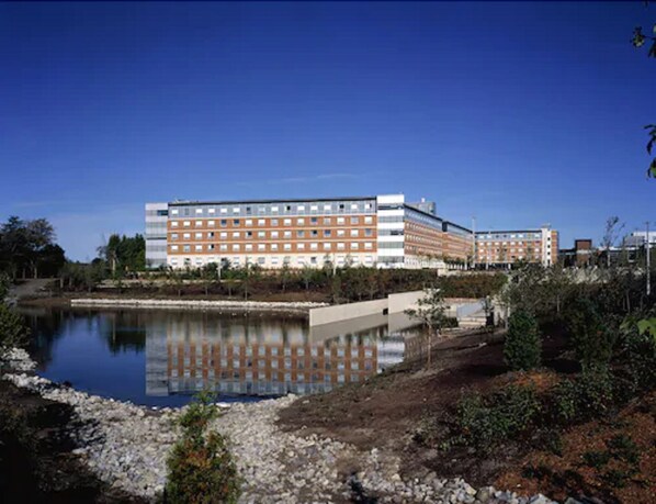 Un hotel con un edificio grande, una piscina reflectante y vegetación circundante.