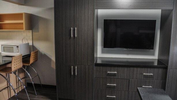 A modern kitchen with dark wood cabinets, a built-in microwave, a flat-screen TV, and a bar area. - Residence & Conference Centre - Kitchener Waterloo (Kitchener)