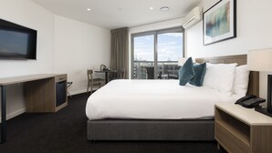 A hotel room with a large bed, a desk, a chair, a TV, and a window with a city view. - Oaks Auckland Hotel (Auckland)
