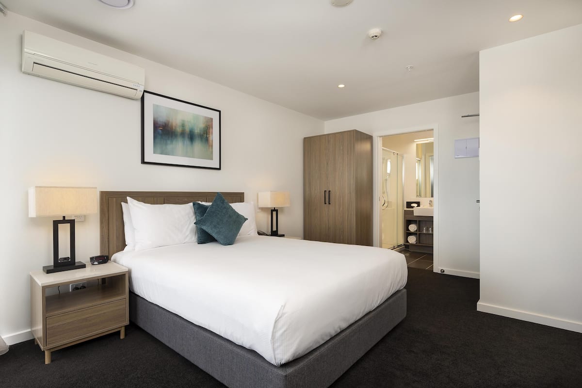 A hotel room with a large bed, bedside tables, a wardrobe, and a bathroom visible through an open door.