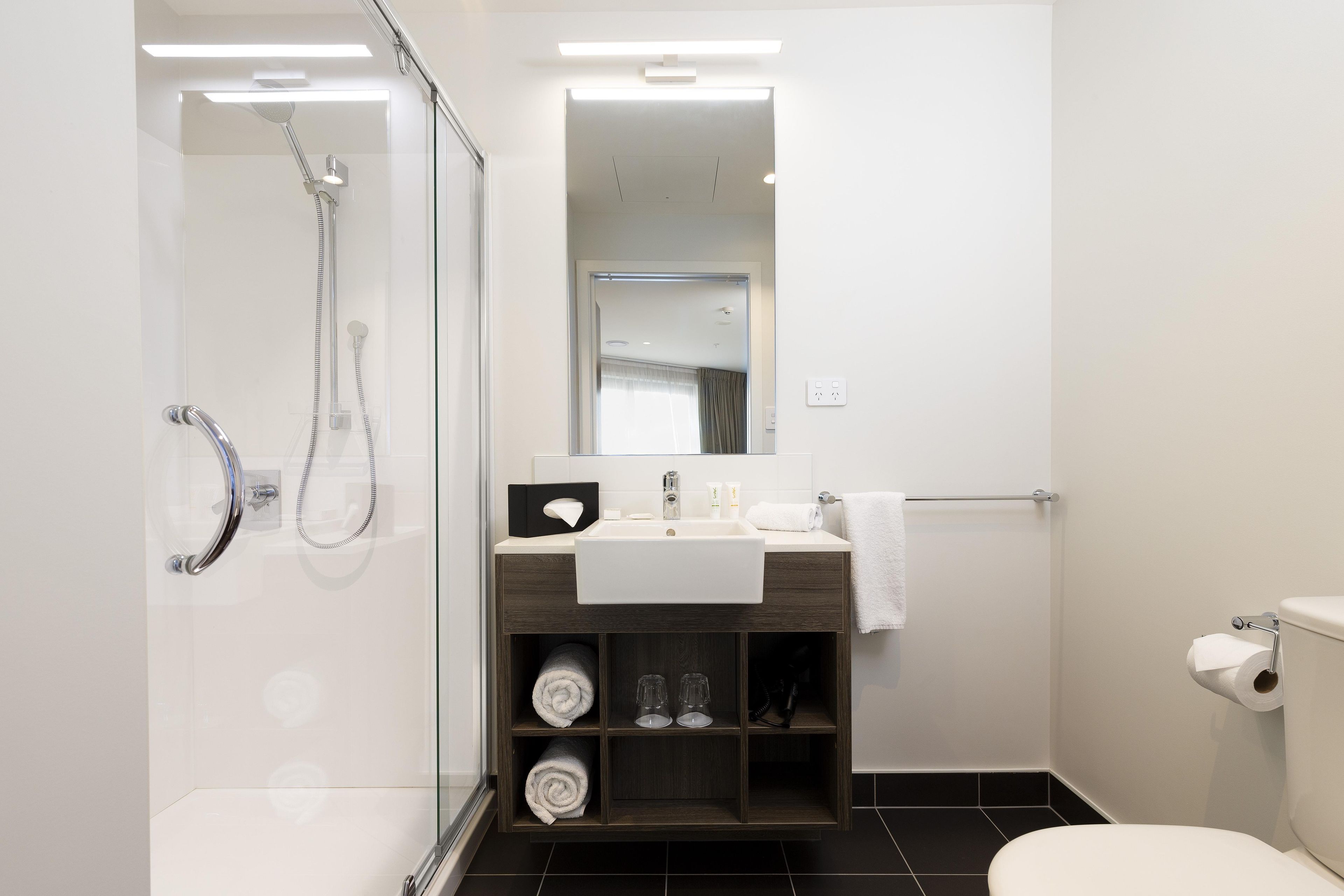 A modern bathroom with a glass-enclosed shower, a sink with a towel rack, and a toilet.
