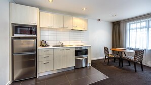 A modern kitchen with stainless steel appliances, a dining area with patterned chairs, and a large window with curtains. - Oaks Auckland Hotel (Auckland)