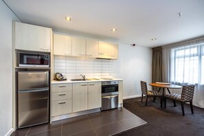 A modern kitchen with stainless steel appliances, a dining area with patterned chairs, and a large window with curtains. - Oaks Auckland Hotel (Auckland)