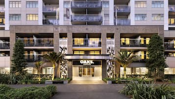 Un hotel de varios pisos con una entrada central, balcones y plantas en el exterior.