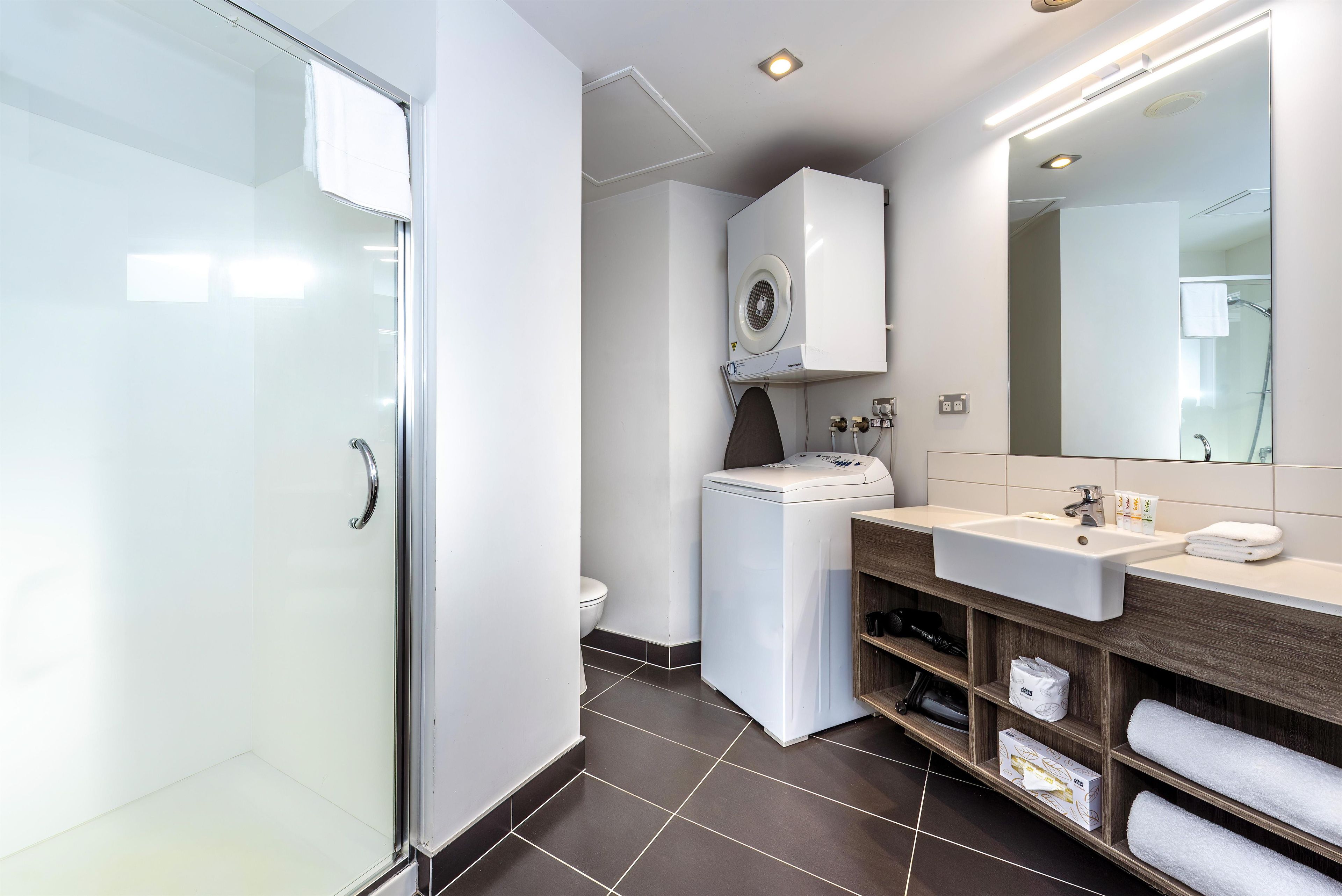 A modern bathroom with a glass shower enclosure, a built-in washing machine, and a vanity with a mirror.