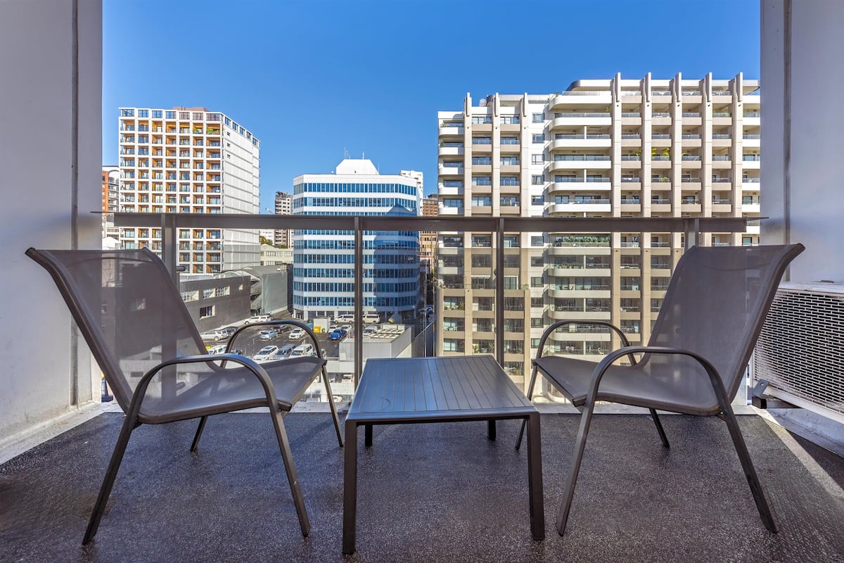 A balcony with two chairs and a table, overlooking a cityscape with modern buildings.
