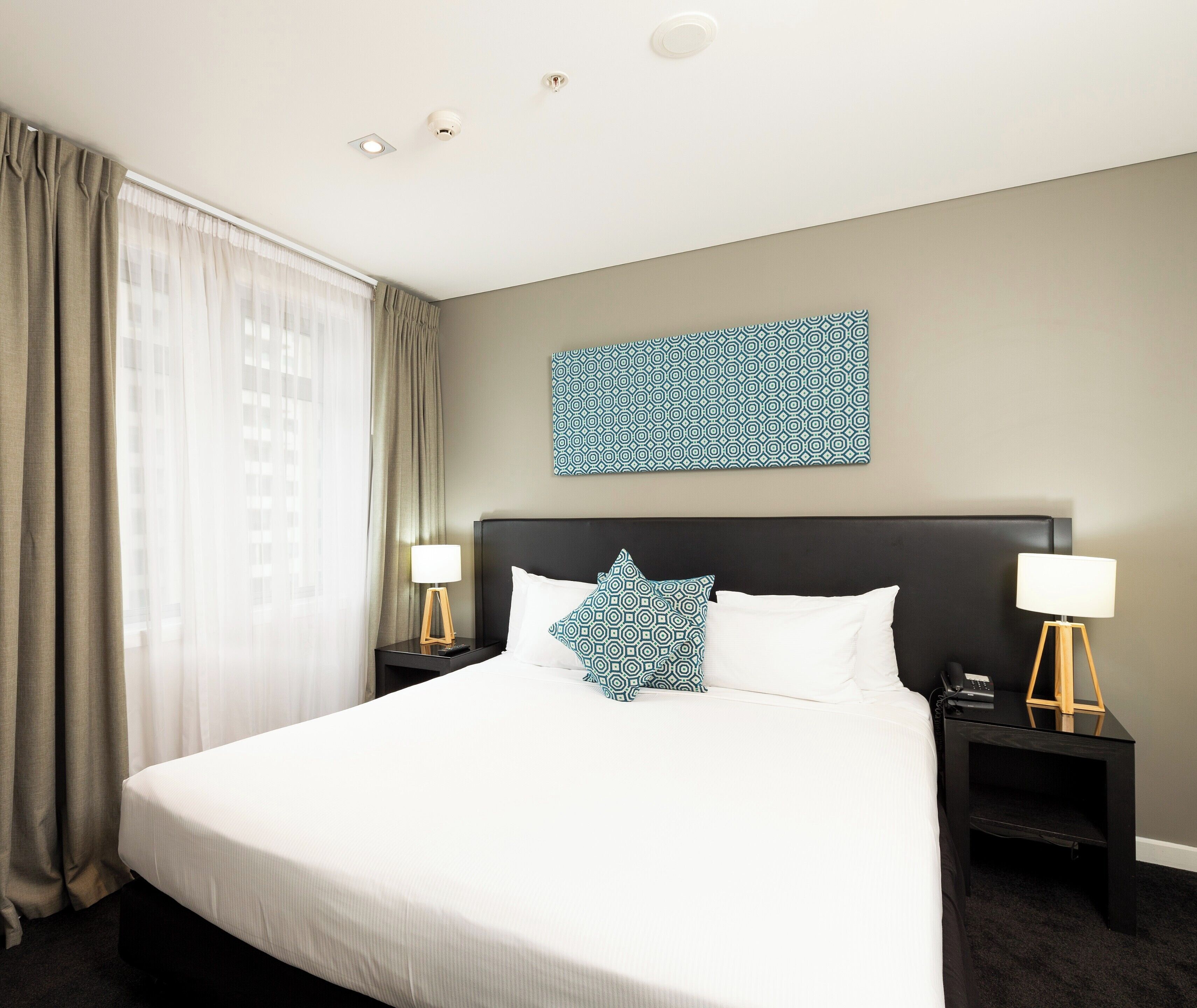 Hotelkamer met een groot bed, twee nachtkastjes, een wandlamp en een raam met gordijnen.